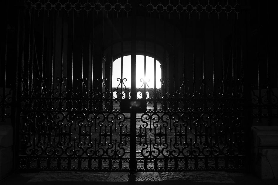 Black and white silhouette of an ornate iron gate with architectural details.