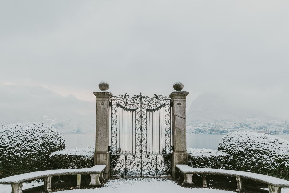 Elegantly wrought iron gate amid snow with a breathtaking view of a foggy lake, perfect for winter themes.